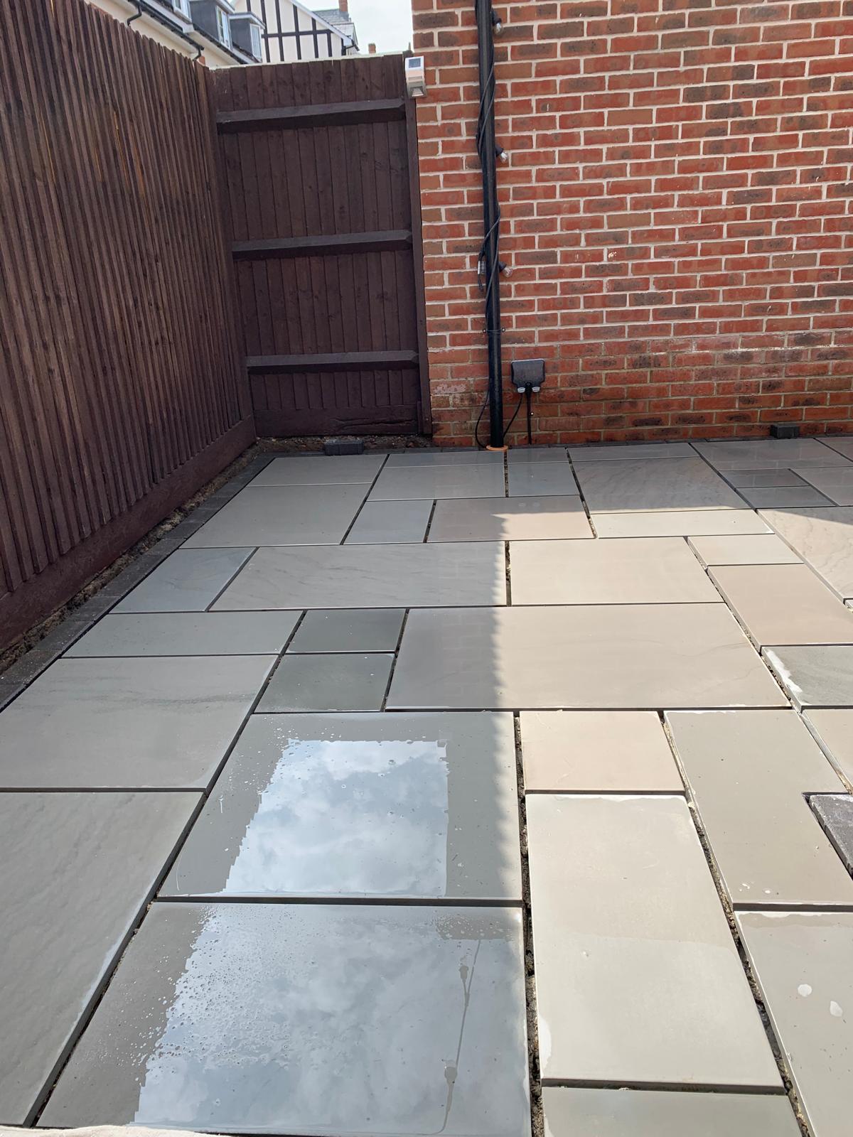 Light stone patio slabs laid between a brick wall and a fence