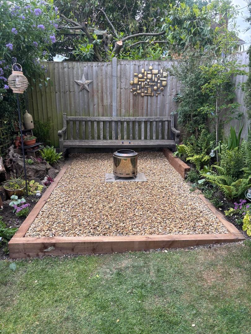 Gravel seating area with a fire pit and a bench, edged with timber